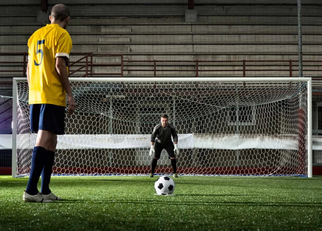 Soccer player preparing for a penalty kick against a goalkeeper on an indoor field.