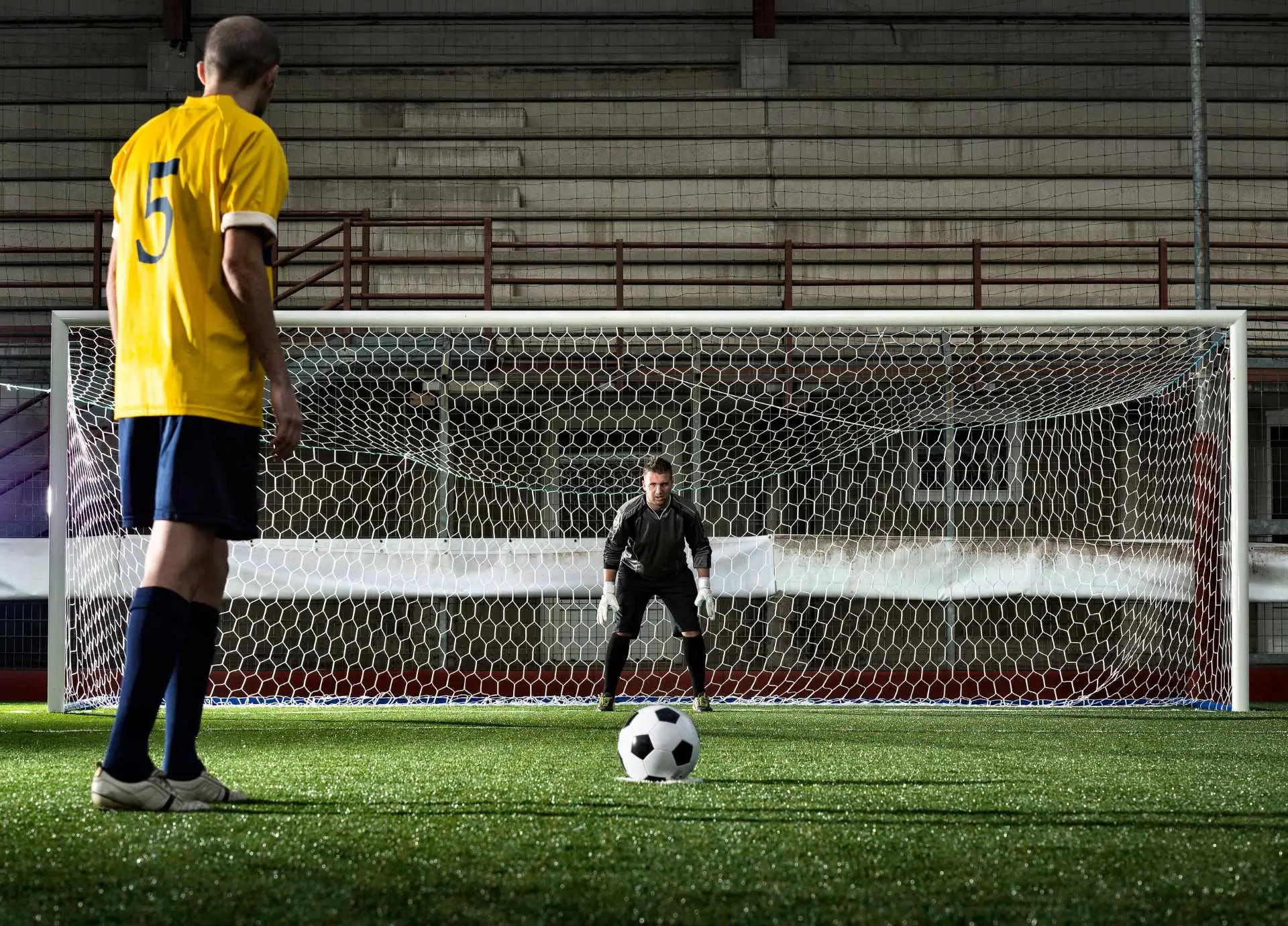 Soccer player preparing for a penalty kick against a goalkeeper on an indoor field.