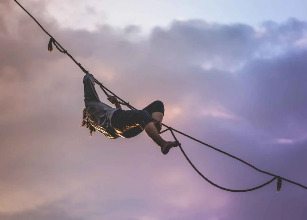 A person balancing on a highline rope against a dramatic, cloudy twilight sky.