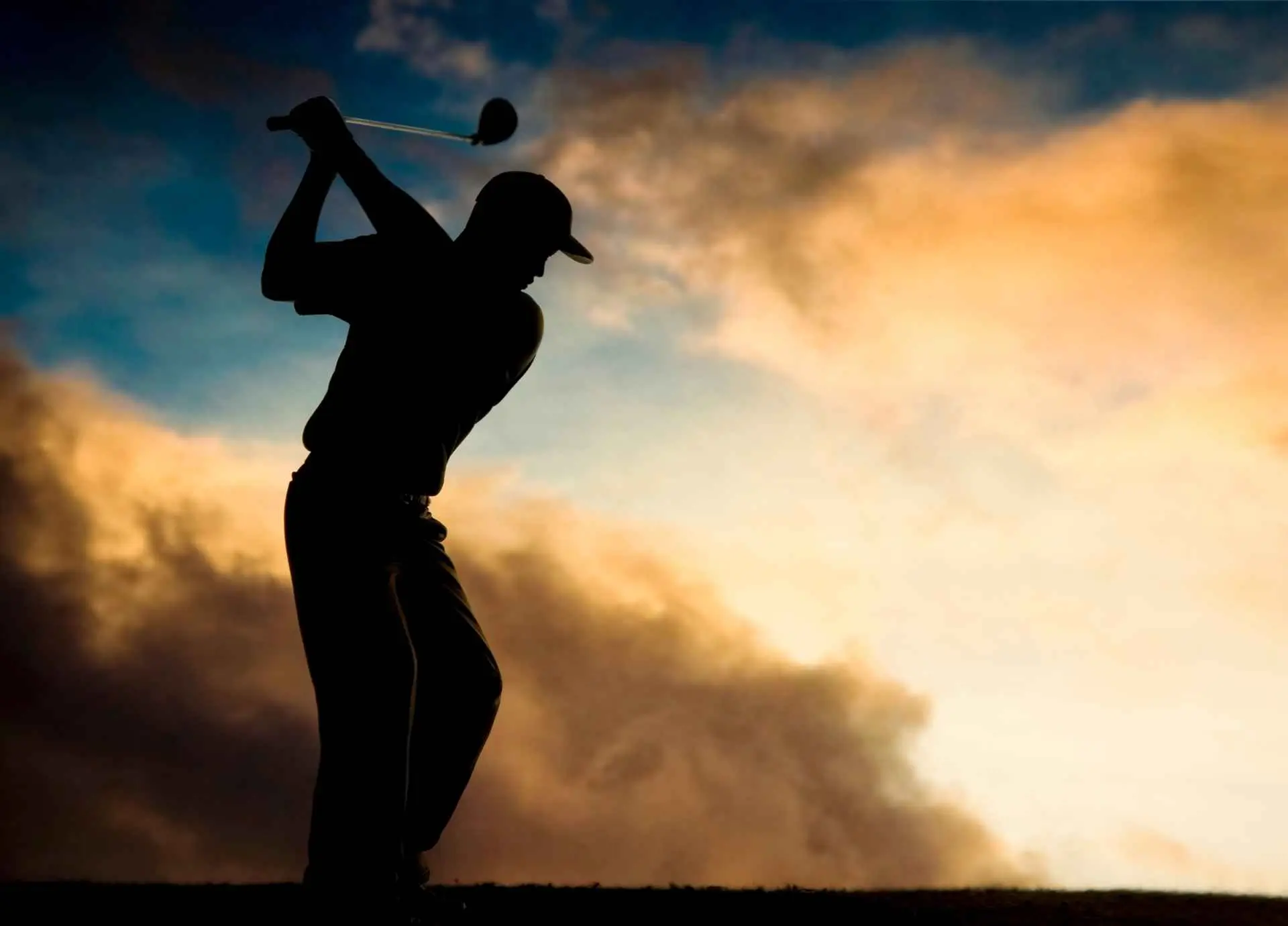 A golfer in silhouette performing a swing against a dramatic, colorful sunset sky.